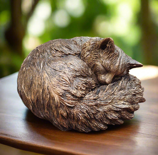 Sleeping cat sculpture curled up on a wooden surface next to a glass door
