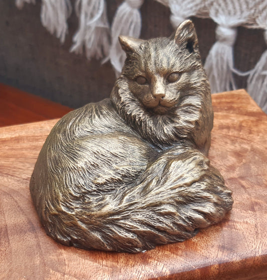 A wooden cremation urn with a bronze effect cat figurine attached to it, set on a wooden surface.