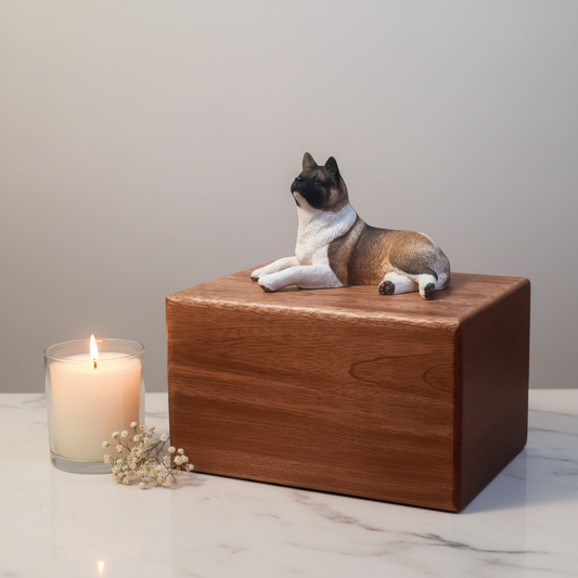 Large Wooden pet urn with a dog figurine on top, accompanied by a candle and small flowers on a marble surface.