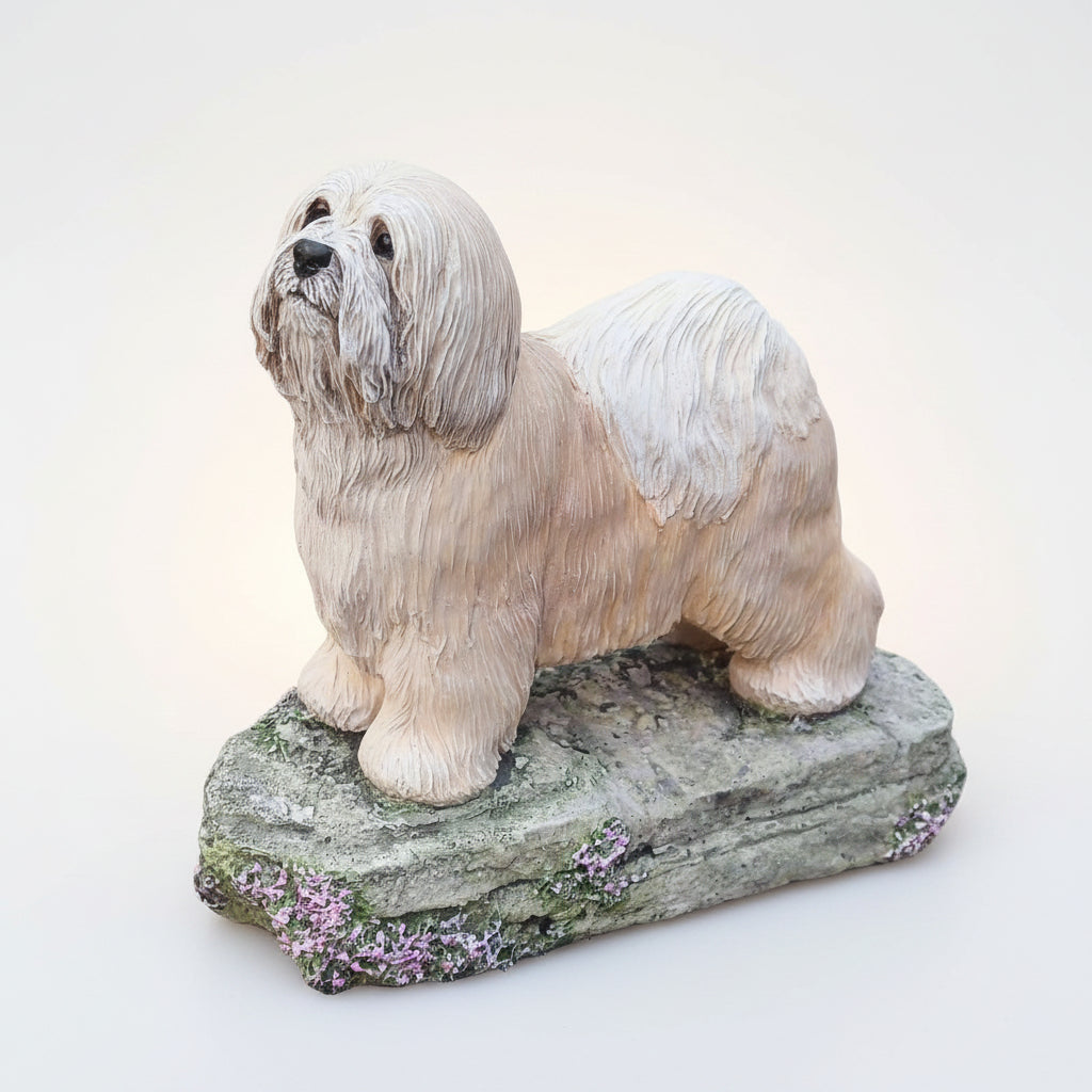 A figurine of a Tibetan Terrier standing on a rock-like base with plants in the background.