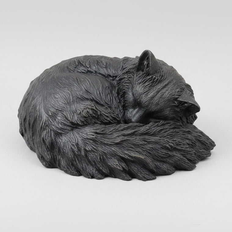 Gray cat figurine on a wooden surface with a plant and artwork in the background
