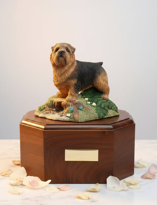 A wooden cremation urn featuring a sculpture of a Norfolk Terrier dog, with a brass inlay on the top edge, placed on a side table.